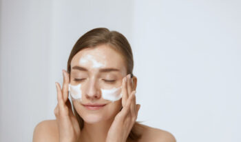 Face skin care. Woman applying facial cleanser on face closeup. Girl using cleansing cosmetic product on skin, washing face on light background