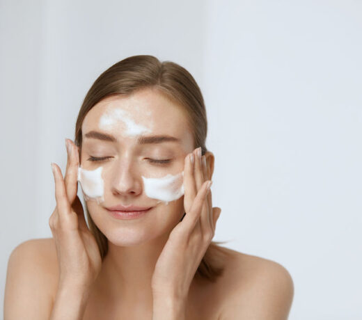 Face skin care. Woman applying facial cleanser on face closeup. Girl using cleansing cosmetic product on skin, washing face on light background